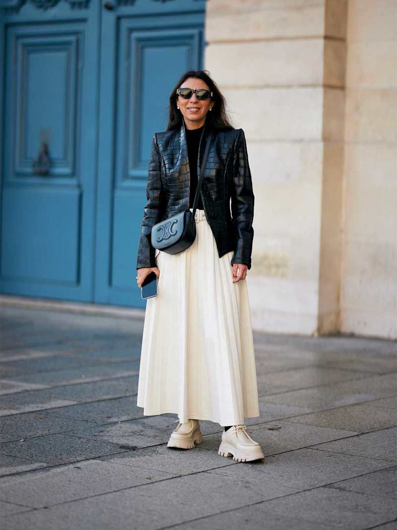 Frau trägt einen cremefarbenen Plisseerock zu einer Lederjacke und Loafers
