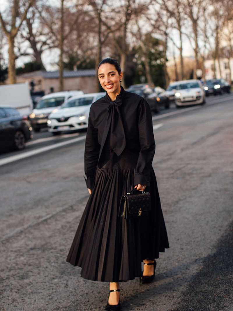 Frau trägt ein All-Black-Outfit bestehend aus Plisseerock und Bluse