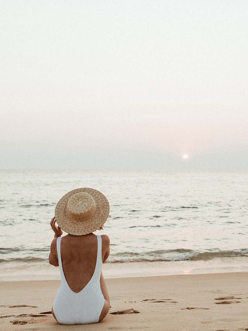 Frau sitzt am Strand und trägt einen weißem Badeanzug