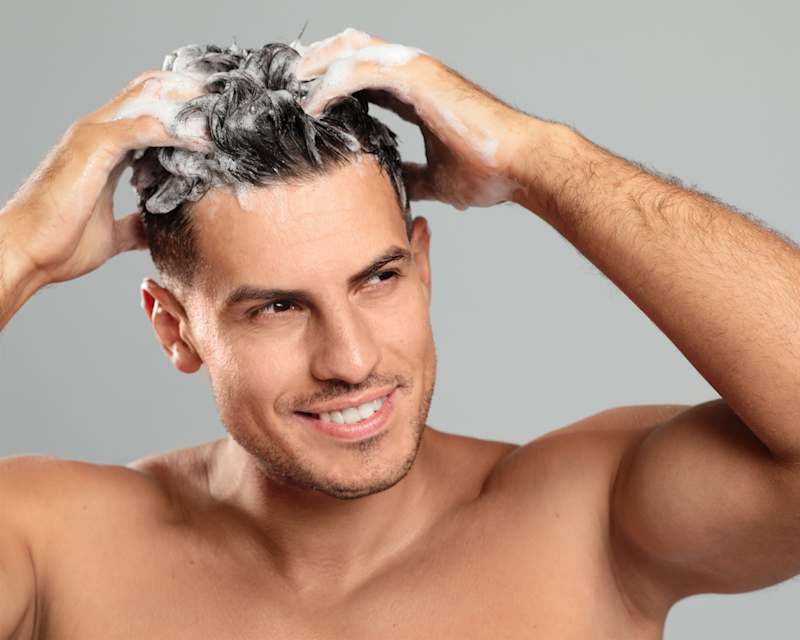Brünetter Mann schäumt sich die Haare mit Shampoo ein
