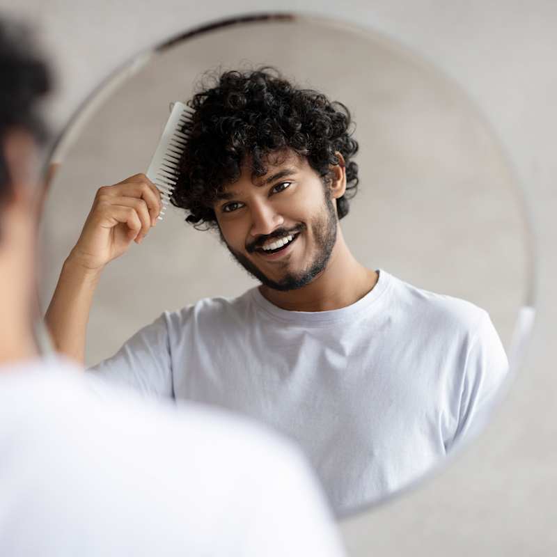 Mann kämmt sich mit Kamm die dunklen Locken im Spiegel