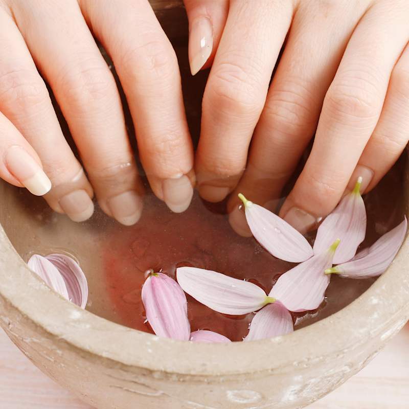 Frau mit langen Nägeln pflegt ihre Nagelhaut und hält ihre Hände in ein Wasserbad