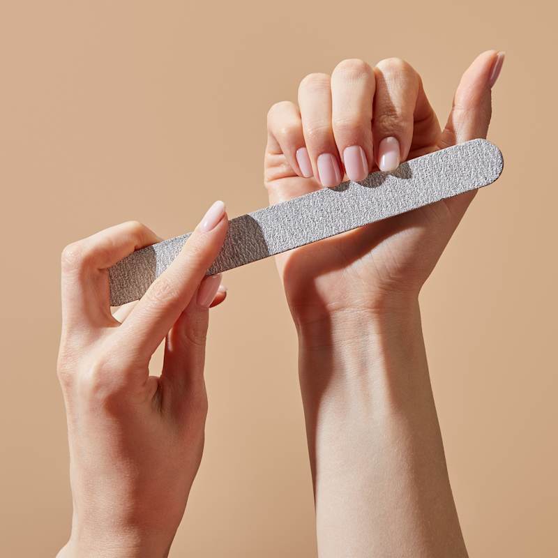 Frau feilt ihre nudefarbenen Nägel mit Nagelfeile