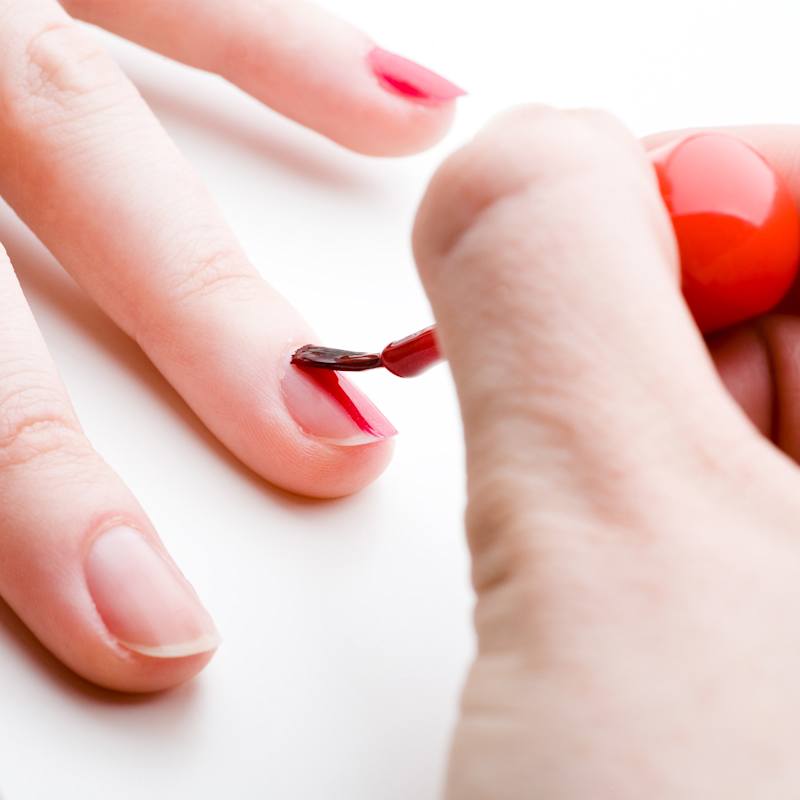 Frau lackiert sich ihre Nägel mit rotem Nagellack