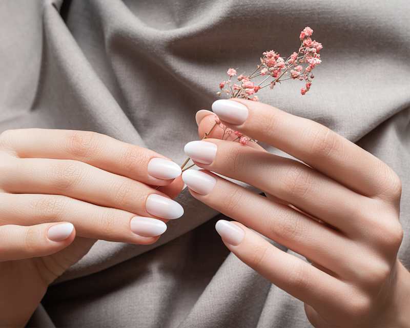 Frau mit gepflegten Nägeln hält rosafarbene Trockenblume in der Hand