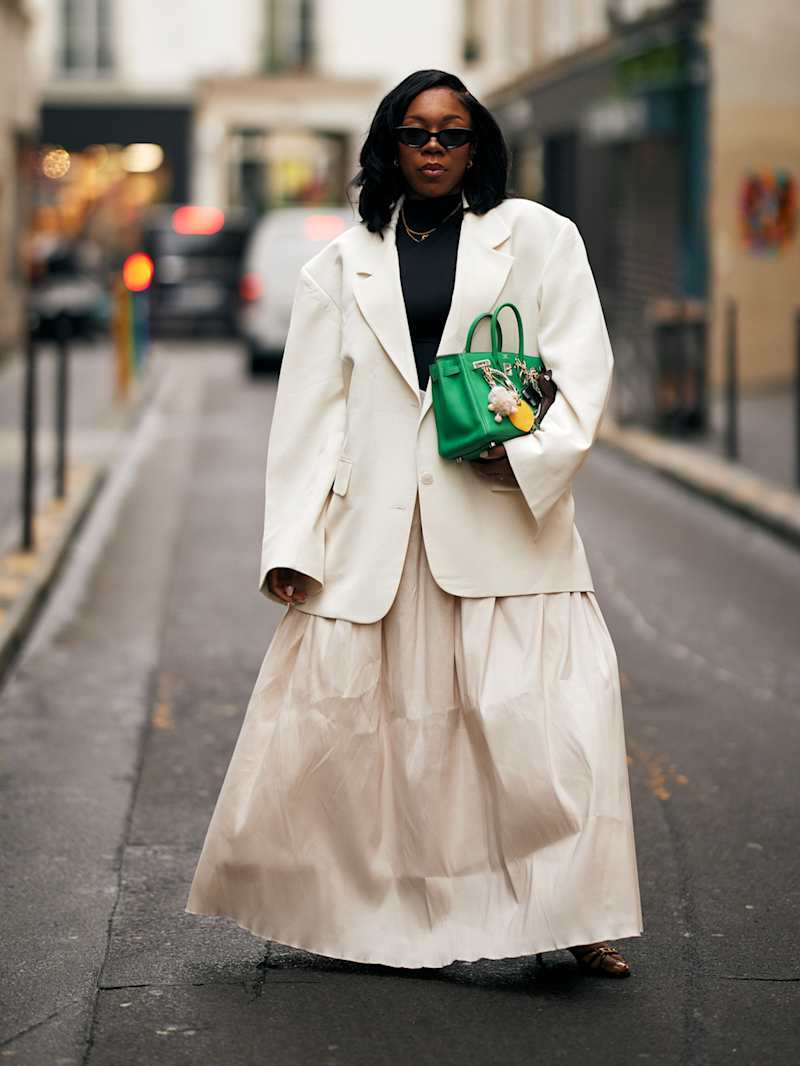 Frau trägt einen Blazer und einen Rock in der Farbe Creme und eine grüne Handtasche mit Bag Charms