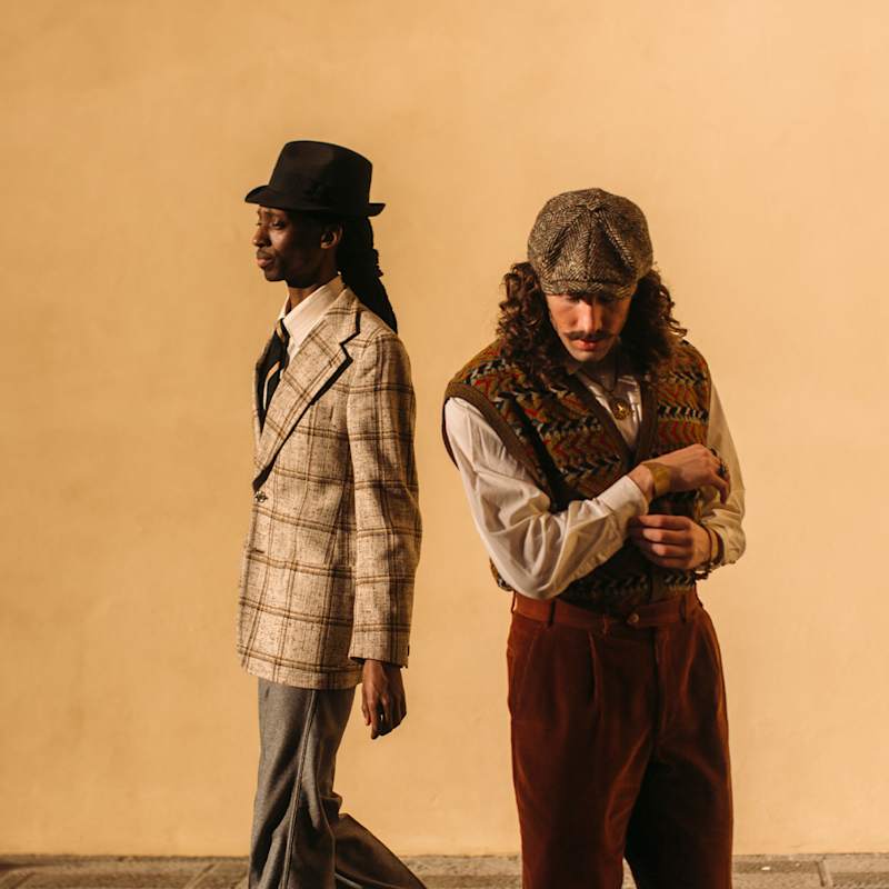 Zwei Männer stehen nebeneinander und tragen karierte Oberteile im Preppy Style