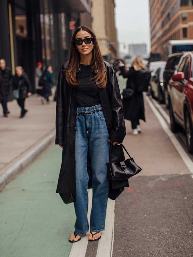 Frau trägt einen schwarzen Mantel und blaue Jeans