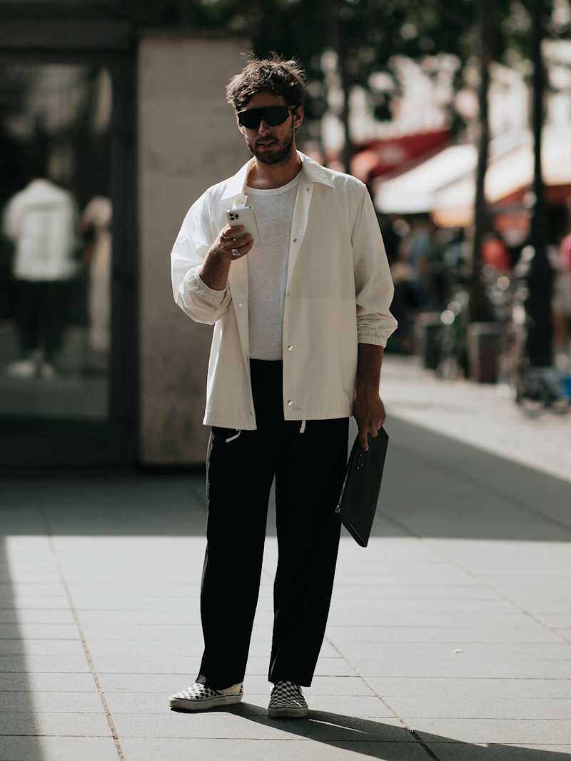 Mann trägt weißes Overshirt, schwarze Hose und eine schwarze Sonnenbrille