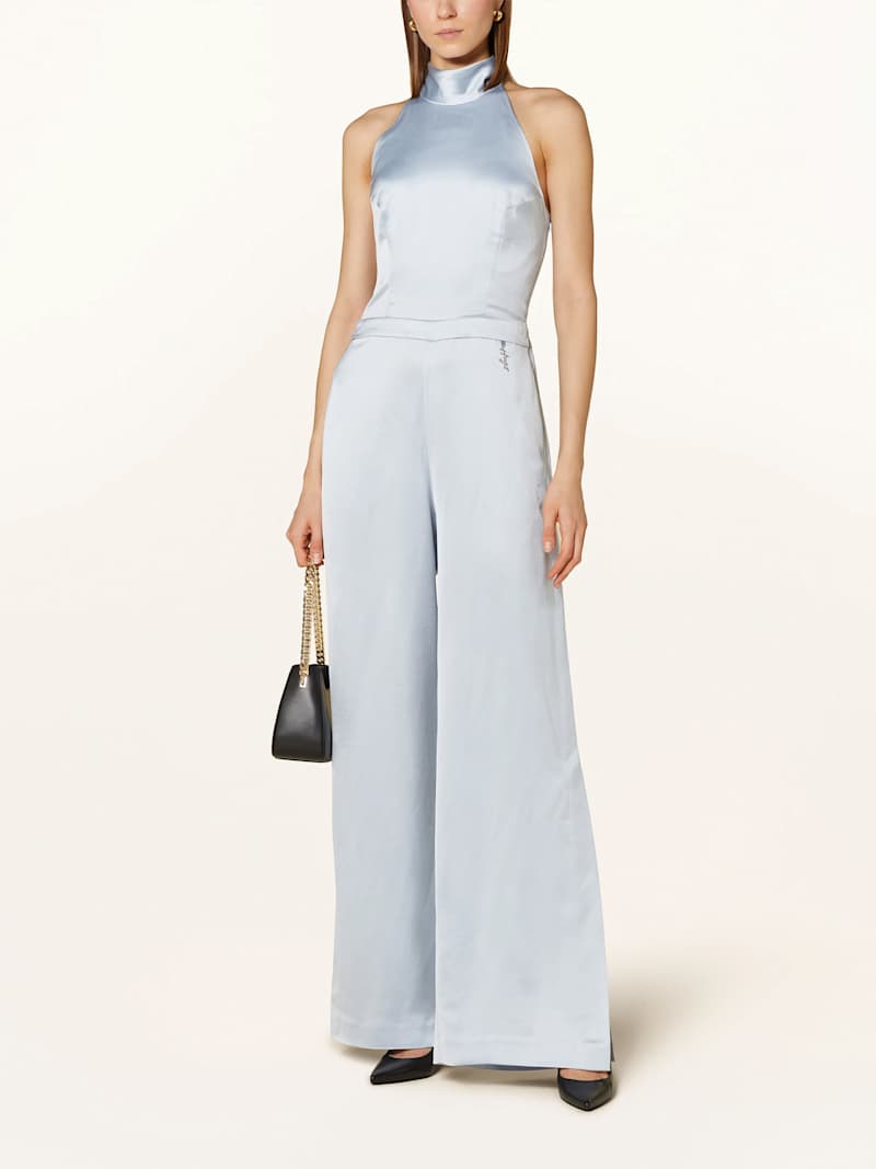 Dunkelblonde Frau trägt hellblauen Satin-Jumpsuit mit Neckholder-Ausschnitt