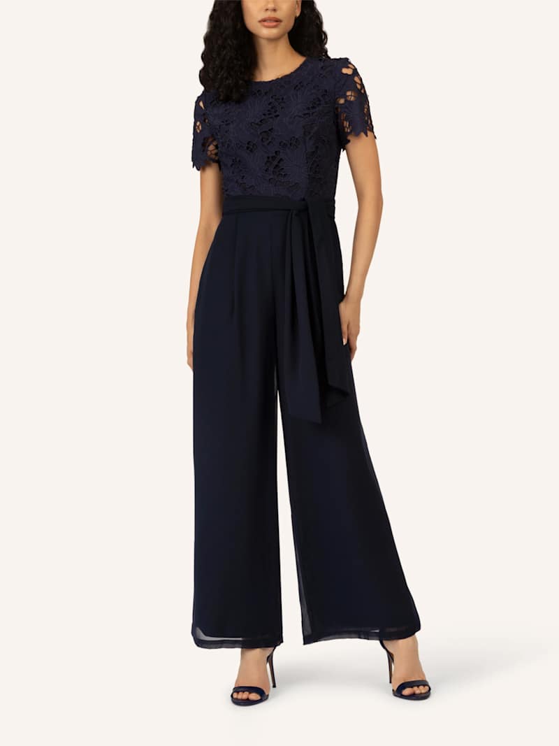 Dunkelhaarige Frau trägt dunkelblauen Jumpsuit mit Spitzeneinsätzen