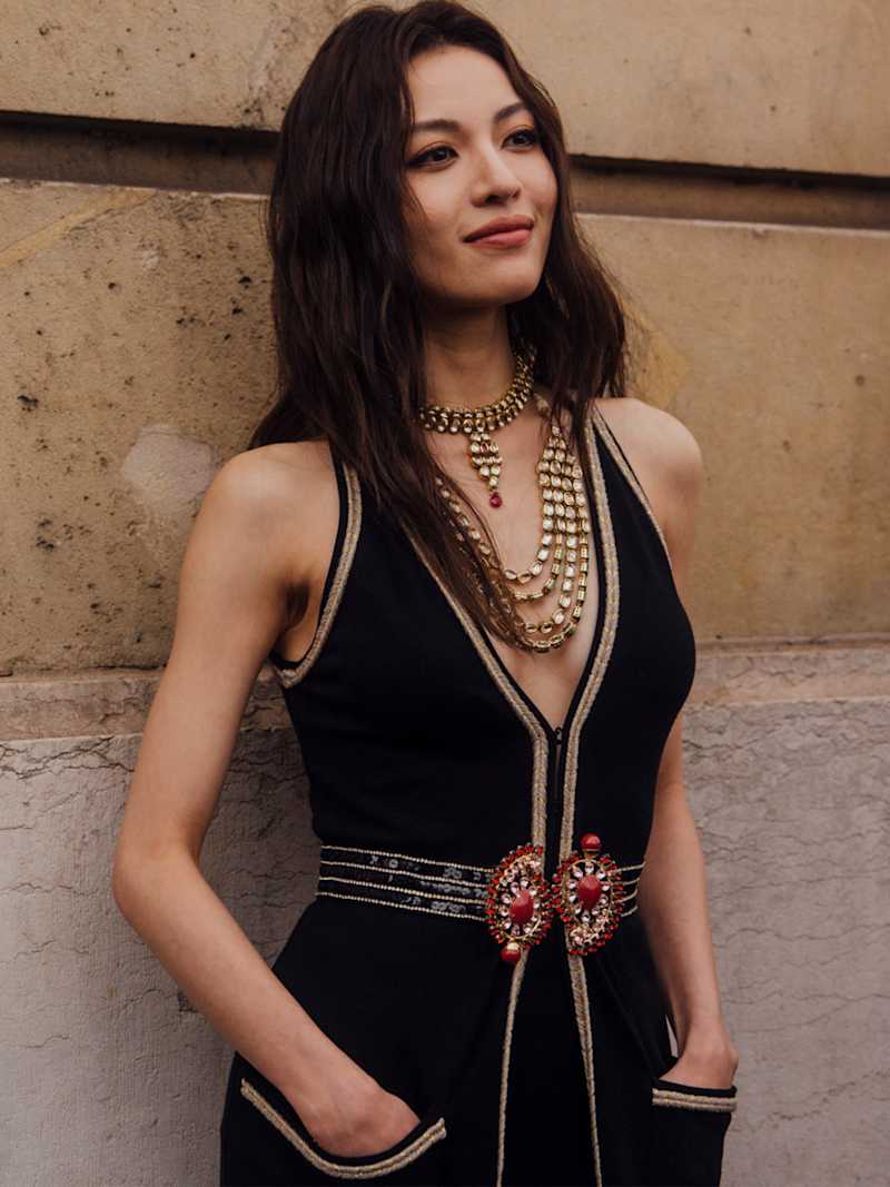 Brünette Frau trägt schwarzen Jumpsuits und auffälligen Goldschmuck