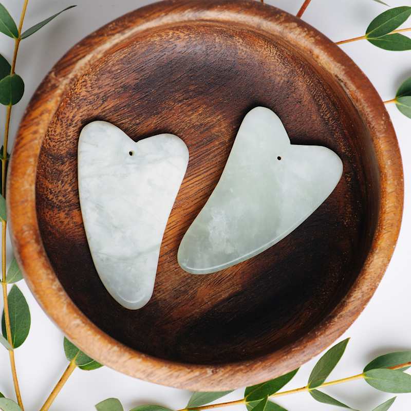 Zwei grüne Gua Sha Steine in einer Holzschale