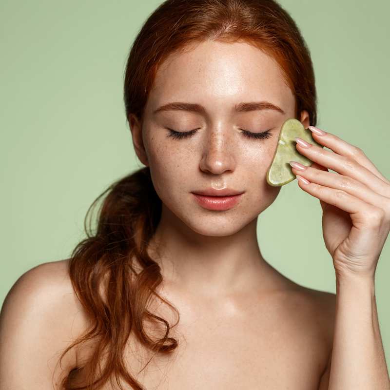 Rothaarige Frau behandelt ihr Gesicht mit einem Gua Sha Stein