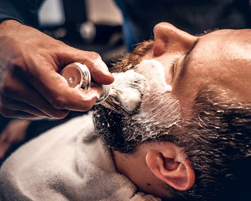 Mann bekommt eine Rasur mit Pinsel und Rasierschaum