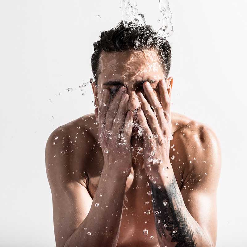 Dunkelhaariger Mann wäscht sein Gesicht mit Wasser