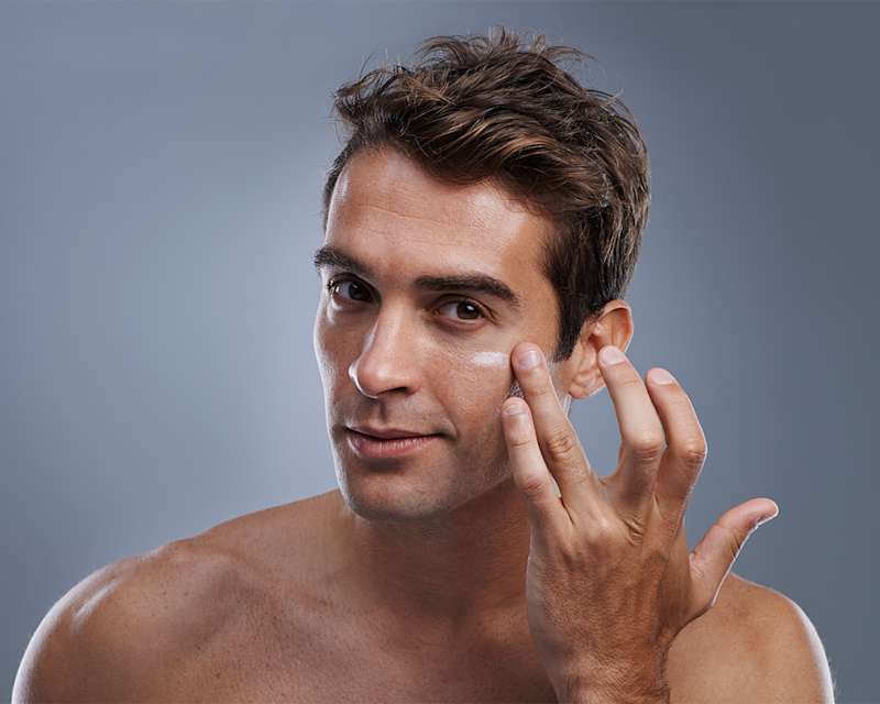 Mann mit braunen Haaren cremt sich die untere Augenpartie ein