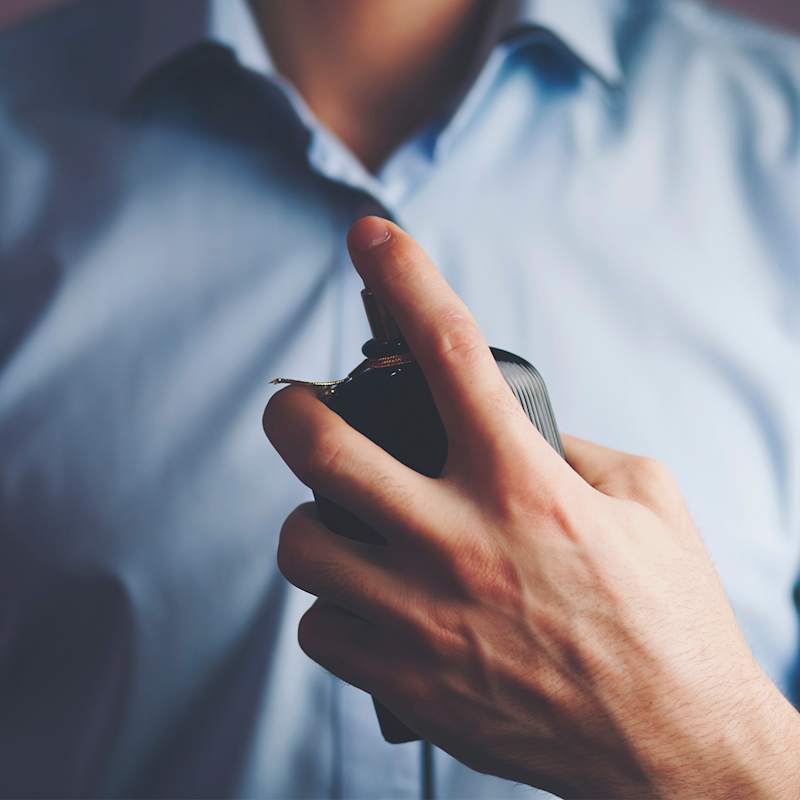 Mann mit hellblauem Hemd trägt einen Duft auf