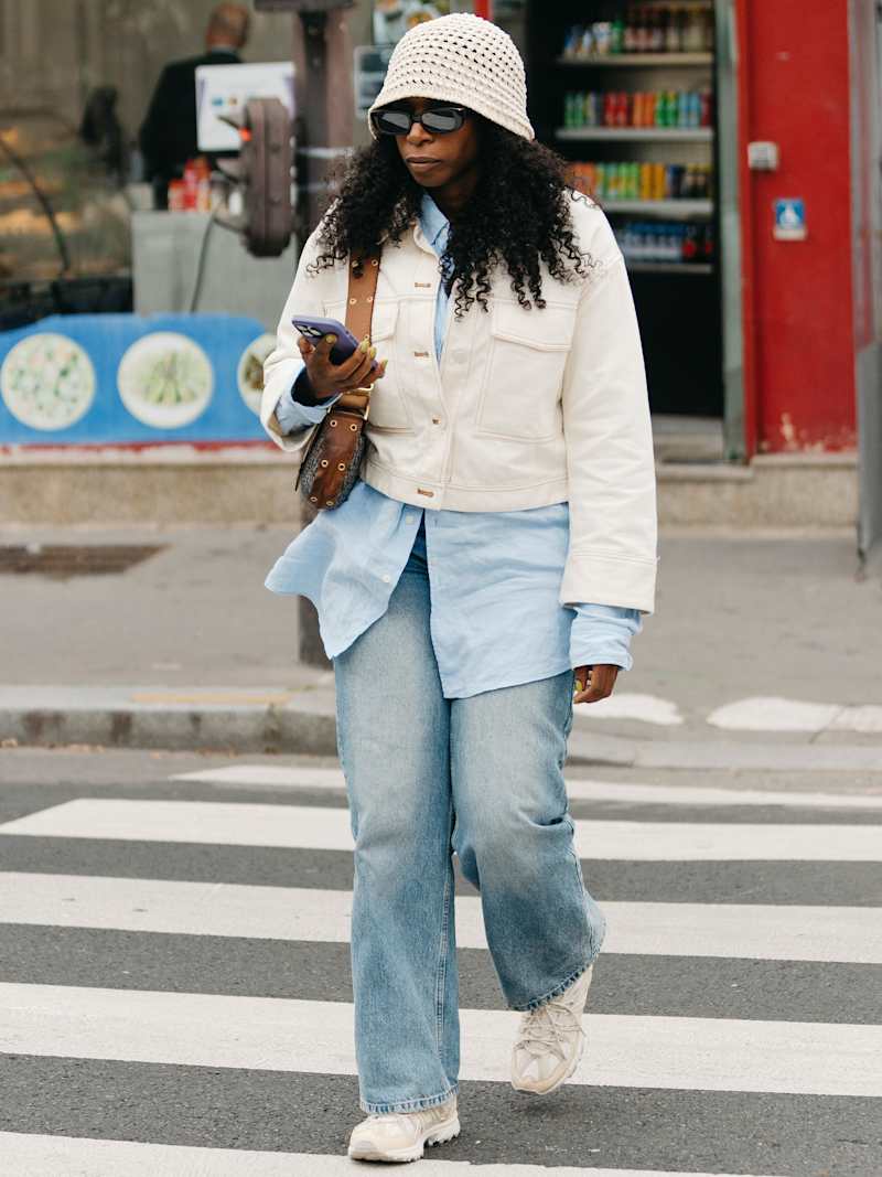 Frau trägt eine cremefarbende Jeansjacke über einer hellblauen Long-Bluse zur einer Jeans mit Stone-Washed-Effekt