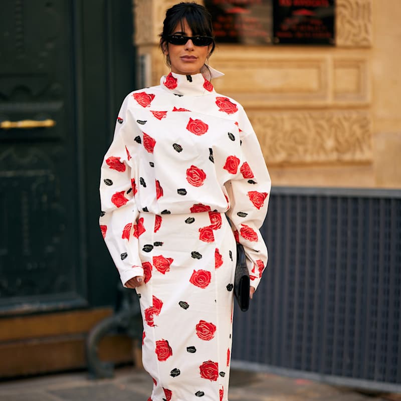 Eine Frau trägt ein weißes Kleid, das mit einem Blumenmuster aus roten Rosen verziert ist