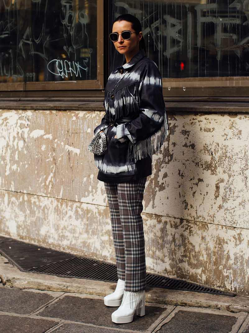 Frau trägt ein schwarz-weißes Batik-Oberteil mit Fransen, dazu eine karierte Hose und weiße Stiefeletten