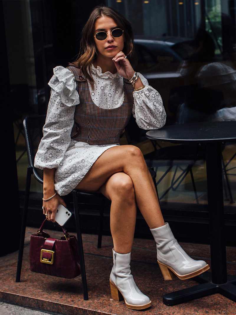 Frau sitzt auf einem Stuhl und trägt ein hellgraues Spitzenkleid, hellgraue Stiefeletten mit Blockabsatz und eine dunkelrote Handtasche