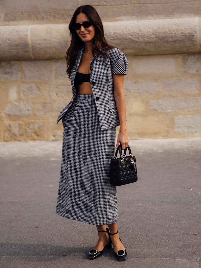 Frau trägt einen Rock und eine Bluse in einem schwarz-weißen Vichy-Karomuster, dazu eine schwarze Lady Dior Handtasche