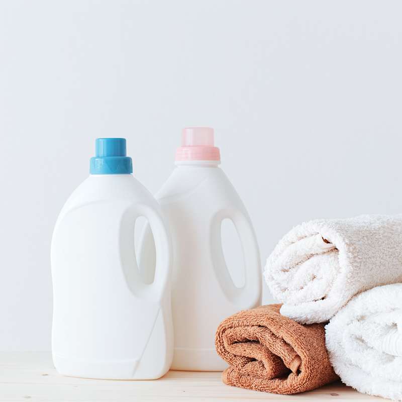 Zwei Flaschen Flüssigwaschmittel neben drei zusammengelegten Handtüchern