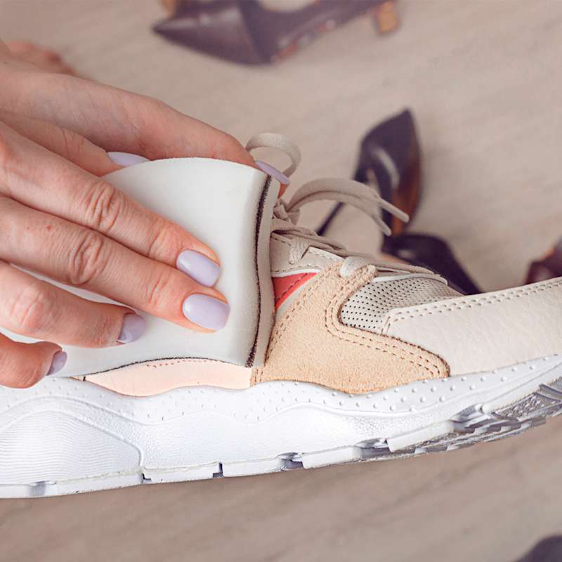 Ein weiß-beiger Sneaker wird händisch mit einem Schwamm abgewischt