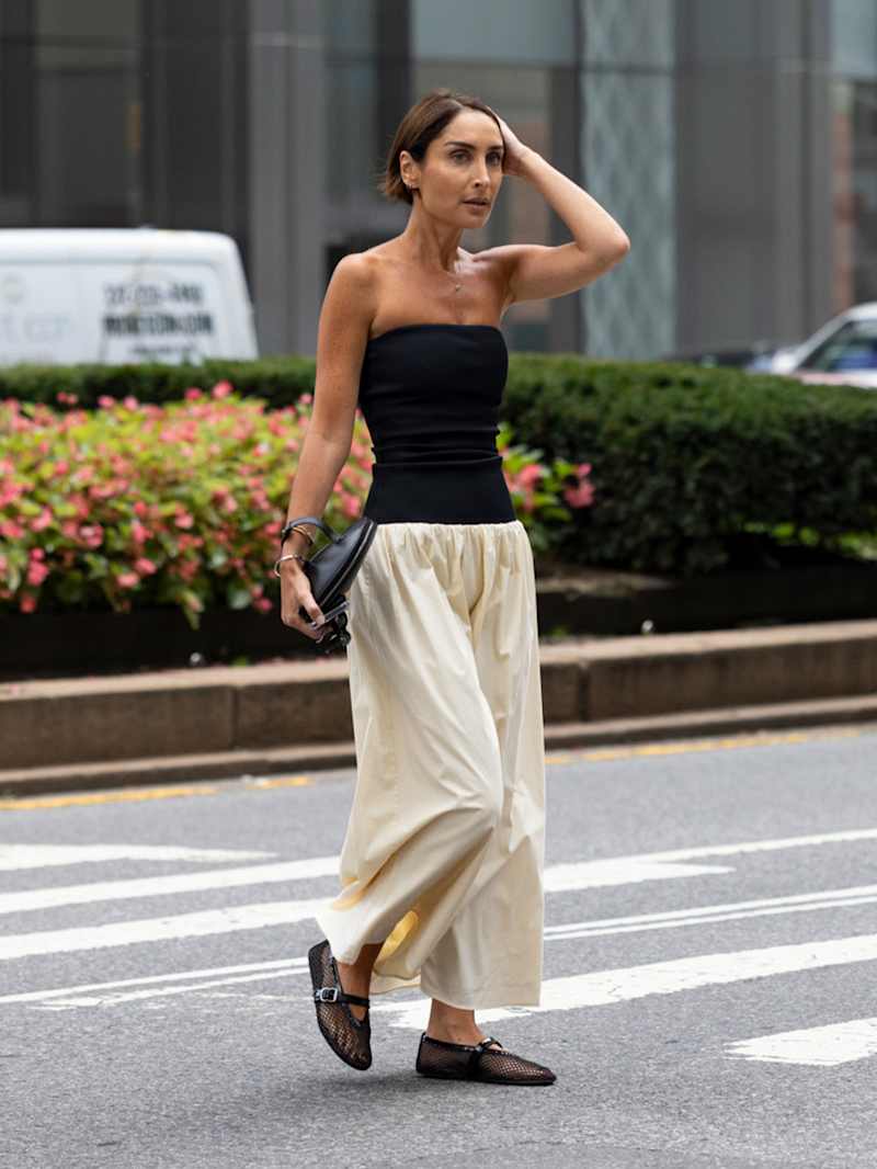 Frau trägt ein schwarzes Top und eine beige Stoffhose zu Mesh-Ballerinas