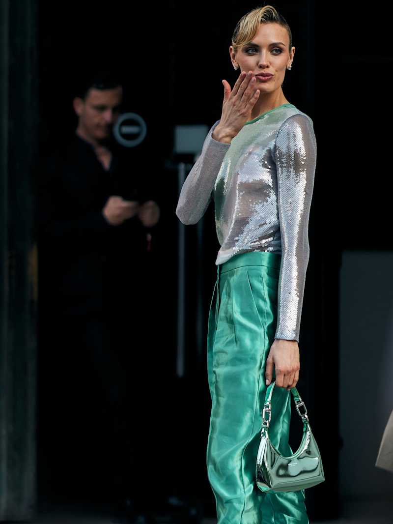 Frau trägt ein silbernes Oberteil zu einer glänzenden grünen Hose und eine Tasche mit Metallic-Finish