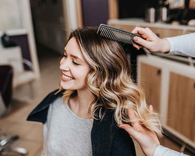 Frau im Friseursalon mit frisch gestylter Balayage, welliges Haar mit sanften Blond-Highlights für natürlichen Look
