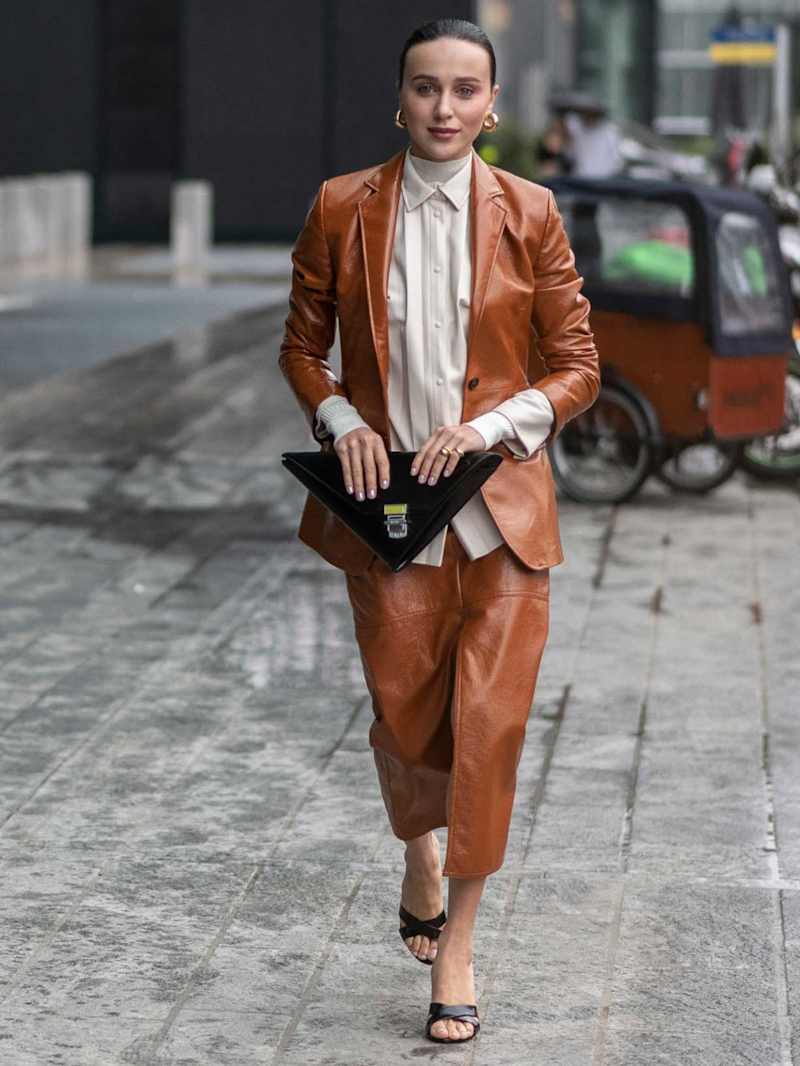 Frau trägt eine Business-Kombination aus Leder zu einer schwarzen Tasche und schwarzen High Heels sowie einer hellen, hochgeschlossenen Blus