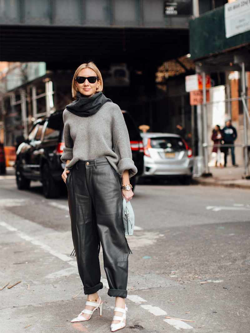 Frau trägt eine Lederhose im Barrel-Fit mit grauem Pullover und hellen High Heels
