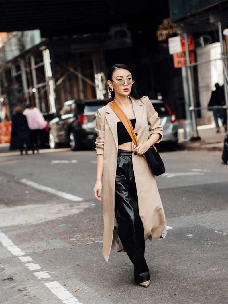 Frau trägt eine weite schwarze Lederhose mit einem schwarzen Tube-Top und einem beigen Trenchcoat