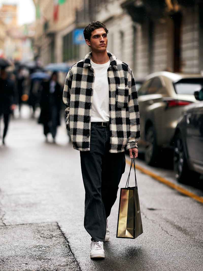 Mann trägt ein schwarz-weiß kariertes Overshirt über einem weißen T-Shirt zu einer schwarzen Jeans und Retro-Sneaker