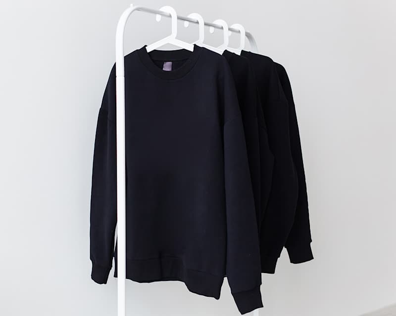 Mehrere dunkle Oberteile hängen auf einer weißen Wäschestange