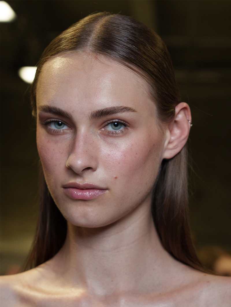 Dunkelblonde Frau mit natürlichem Glow-Make-up, betonten Brauen und Gloss-Lippen