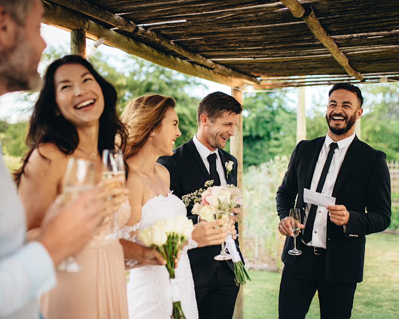 Hochzeitsgast in einem schwarzen Anzug mit Krawatte zusammen mit Brautpaar auf einer Hochzeit