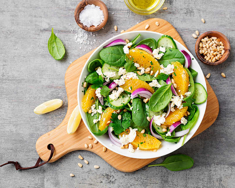 Salatschüssel auf Holzbrett mit Salz, Zitronen und Pinienkernen