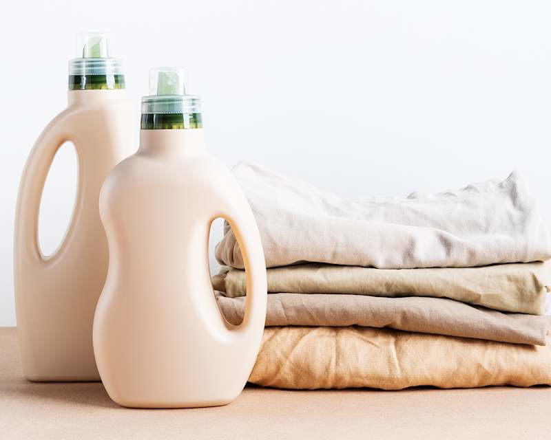 Zwei Waschmittelflaschen aus Plastik stehen neben gefalteter Wäsche.