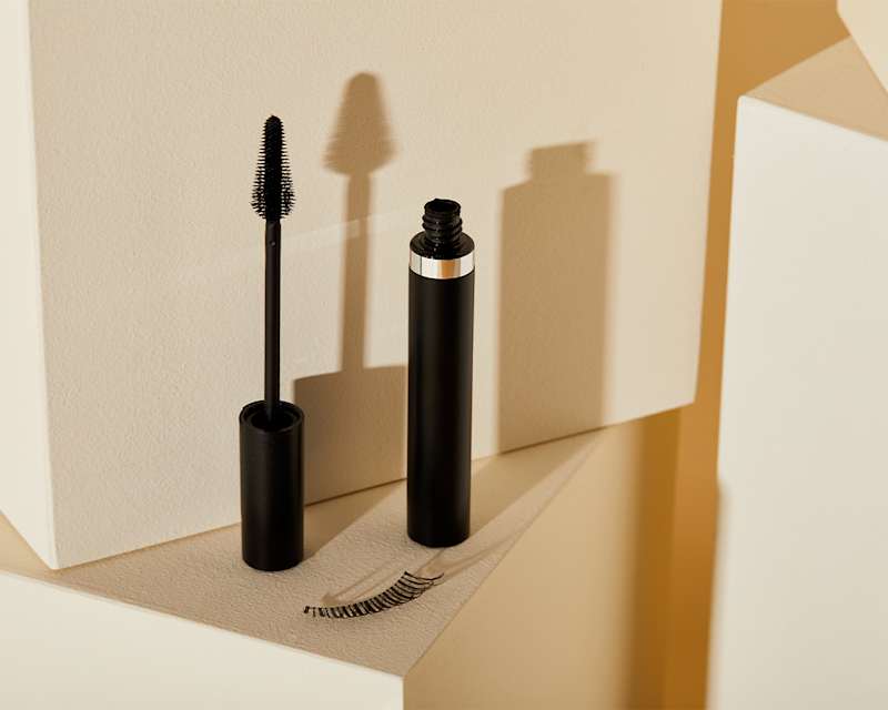 Eine geöffnete schwarze Wimperntusche auf beigem Hintergrund.