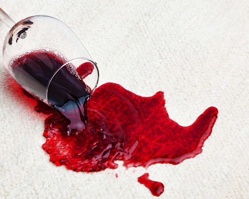 Ausgelaufenes Glas Rotwein auf cremefarbenem Teppich