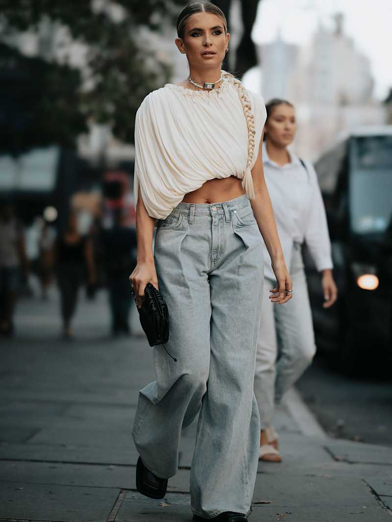 Frau trägt ein weißes Top zu einer Jeans und eine Clutch