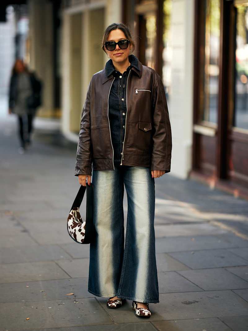 Frau trägt eine Jeans mit heller Waschung in der Mitte der Beine, dazu eine braune Jacke sowie Tasche und Schuhe mit Kuhfell-Muster