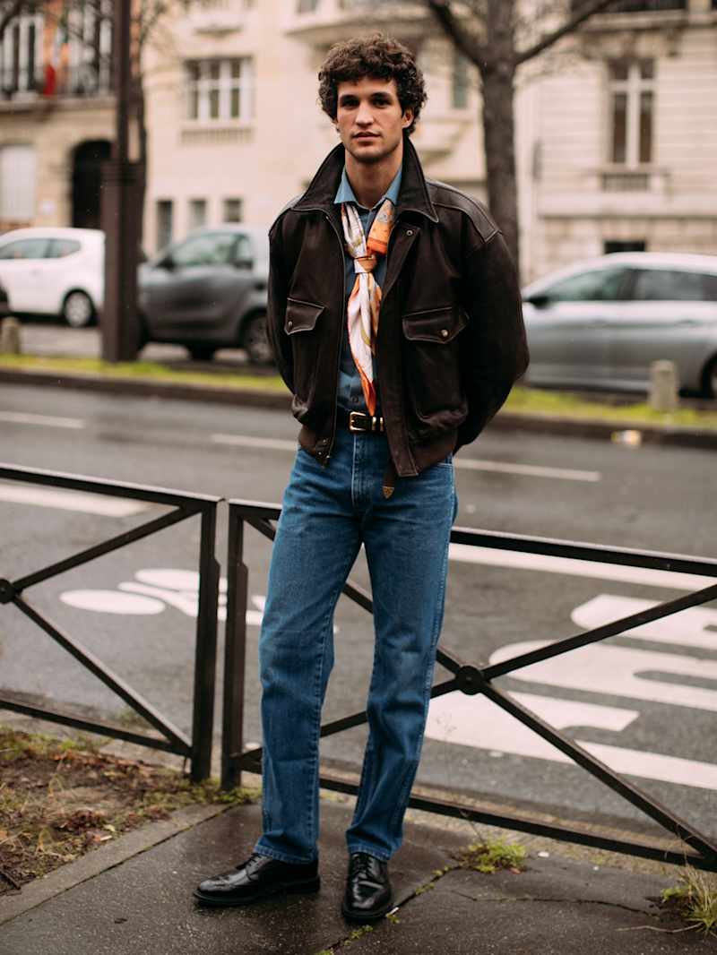 Mann in blauer Jeans mit brauner Lederjacke und einem bunten Halstuch