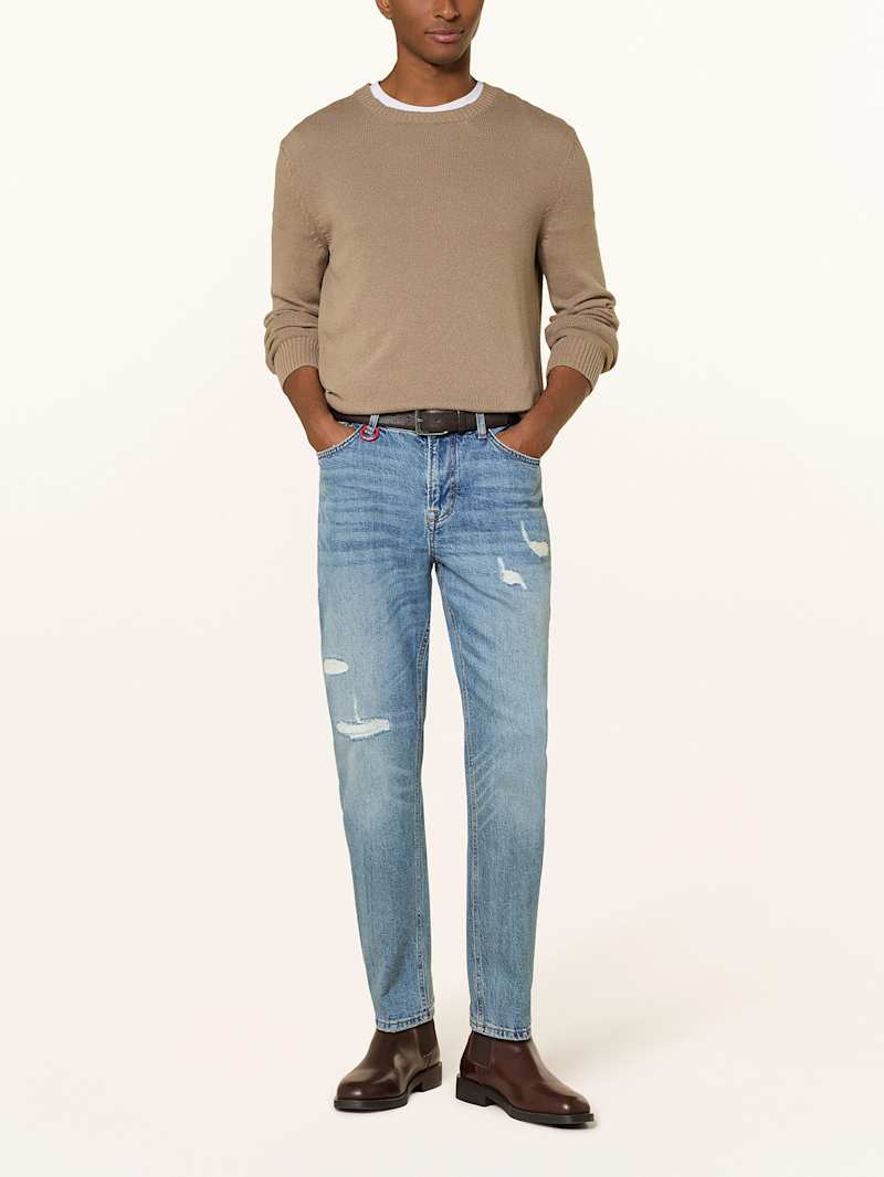 Mann trägt eine blaue Tapered-Fit-Jeans zu einem beigen Pullover
