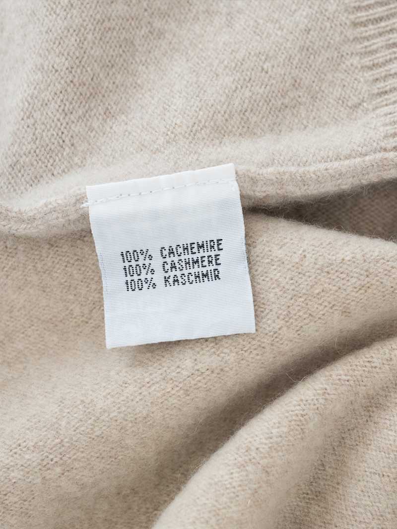 Nahaufnahme von einem hellen Strickpullover mit Etikett auf dem 100 Prozent Kaschmir steht