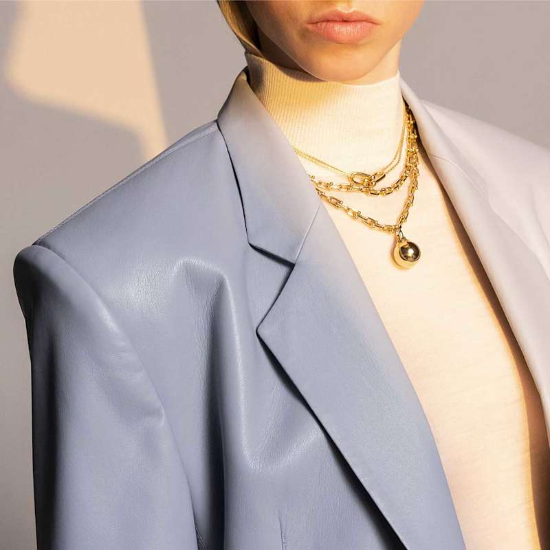 Frau in einem blauen Blazer trägt den angesagten Schmucktrend Ketten-Layering