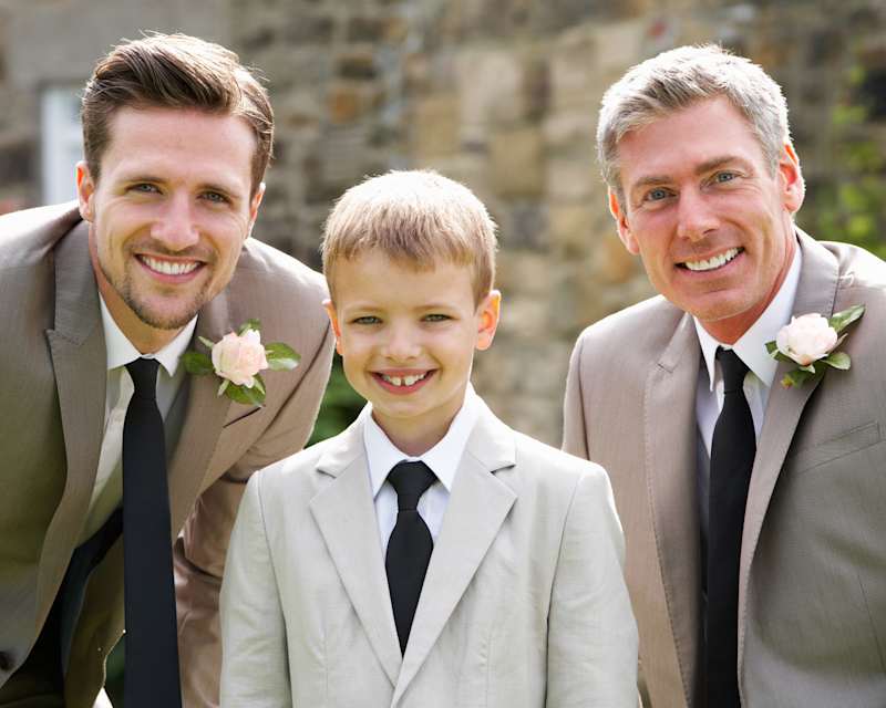 Ein Junge steht in der Mitte von zwei Männern, alle drei tragen graue Anzüge